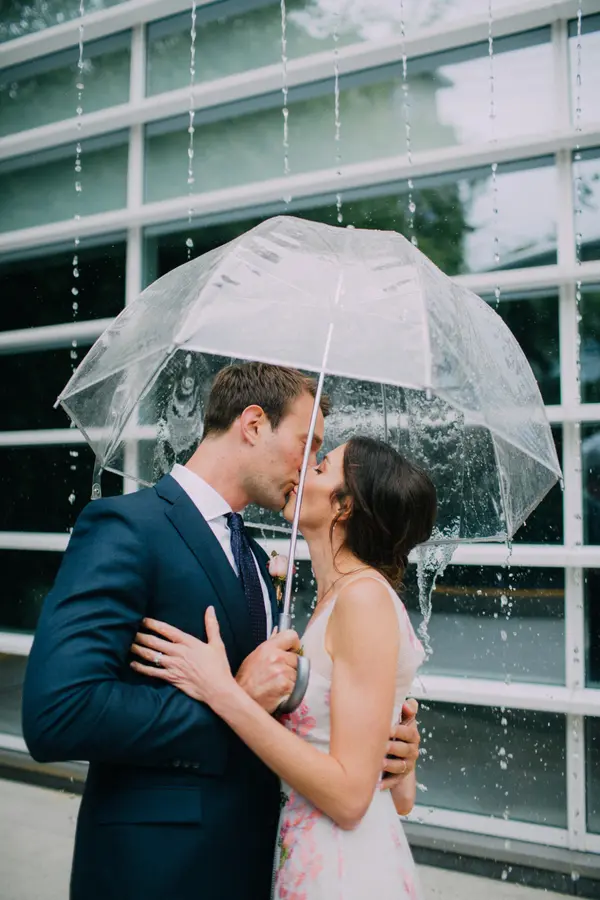 Bride and groom kissing in rain under umbrella at outdoor Pacific Northwest wedding. Lovely Events.
