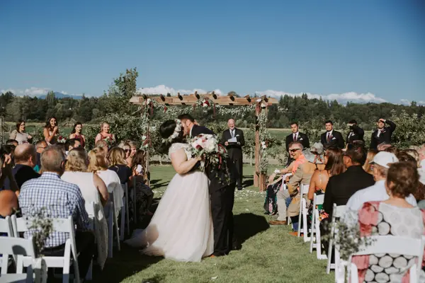 Bride and groom kissing under floral wedding arch at outdoor Washington wedding ceremony. Lovely Events.