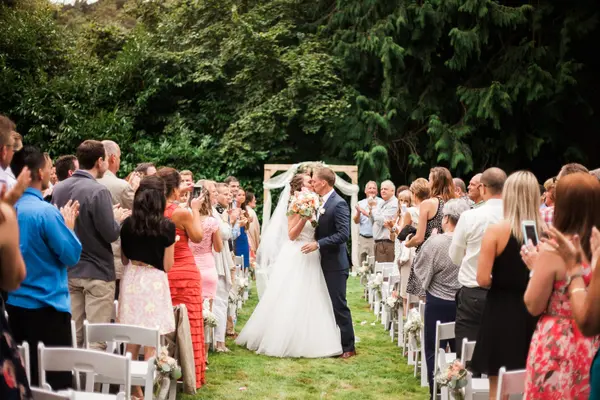 Bride and groom kissing at outdoor Washington wedding ceremony with floral arbor and guests. Lovely Events.