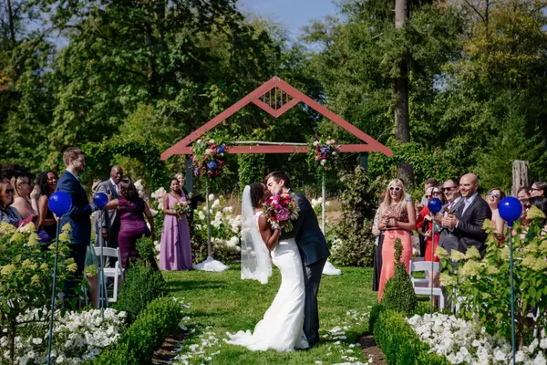 Bride and groom kissing under floral arch at outdoor Pacific Northwest wedding ceremony. Lovely Events.